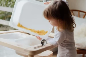 a young child pouring macaroni noodles into a bin