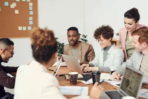 young professional adults sitting around a table with laptops, having a conversation