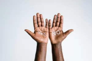 A man's hands, palm side up. One hand has "yes" written in white words and the other hand has "no" written in white words.