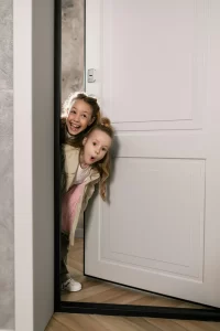 Two young girls who are standing in a doorway with silly, sneaky smiles