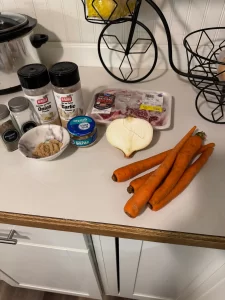 Carrots, half an onion, and bottles of seasoning sitting on a white kitchen counter top.