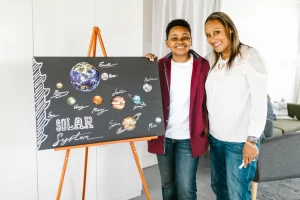 A mother with her preteen standing beside a solar system posterboard, representing the teach back facilitation homeschool technique