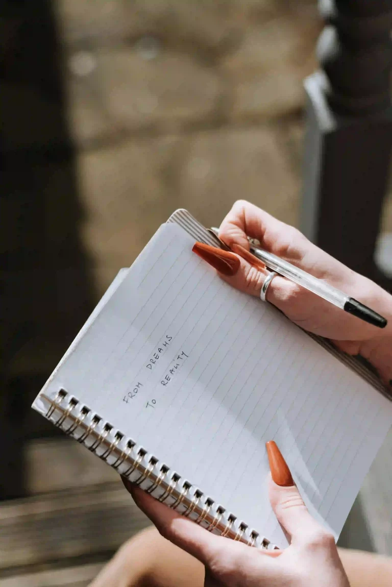 a woman with auburn painted nails, holding a pen and notepad