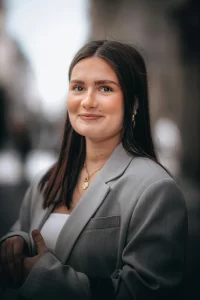 a woman with dark brown hair, wearing a gray suit jacket and smiling into the camera