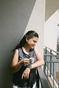 A woman smiling on a porch with a cup of coffee