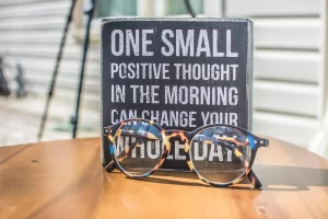 A plaque that reads "One small positive thought in the morning can change your whole day". There's a pair of reading glasses sitting on the table in front of the sign.