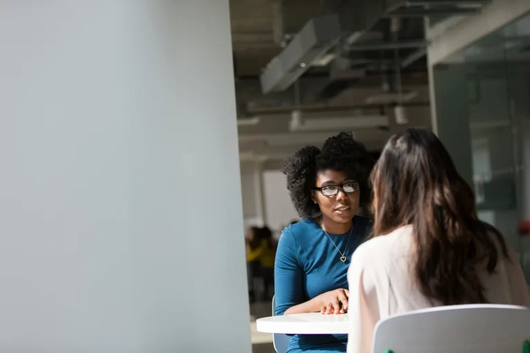 two women sitting at a small table, in conversation