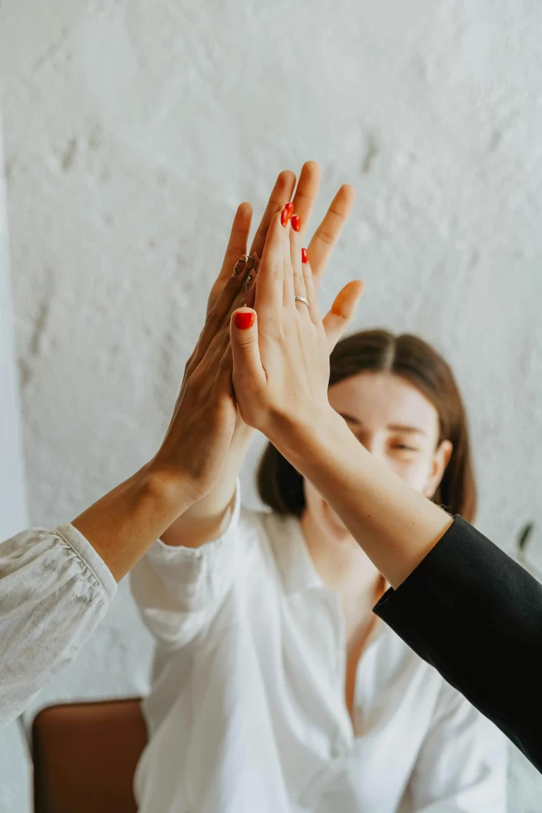 Three hands in the air, high-fiving. One woman's smiling face is shown.