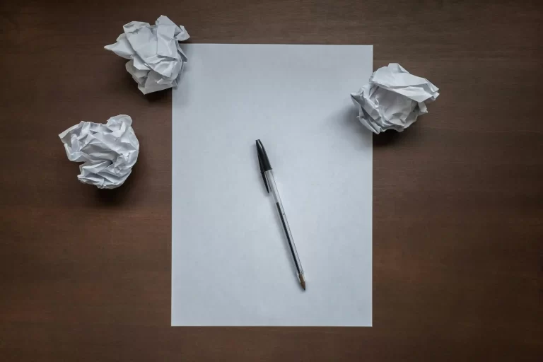 A blank piece of paper, a pen and three balled up sheets of paper