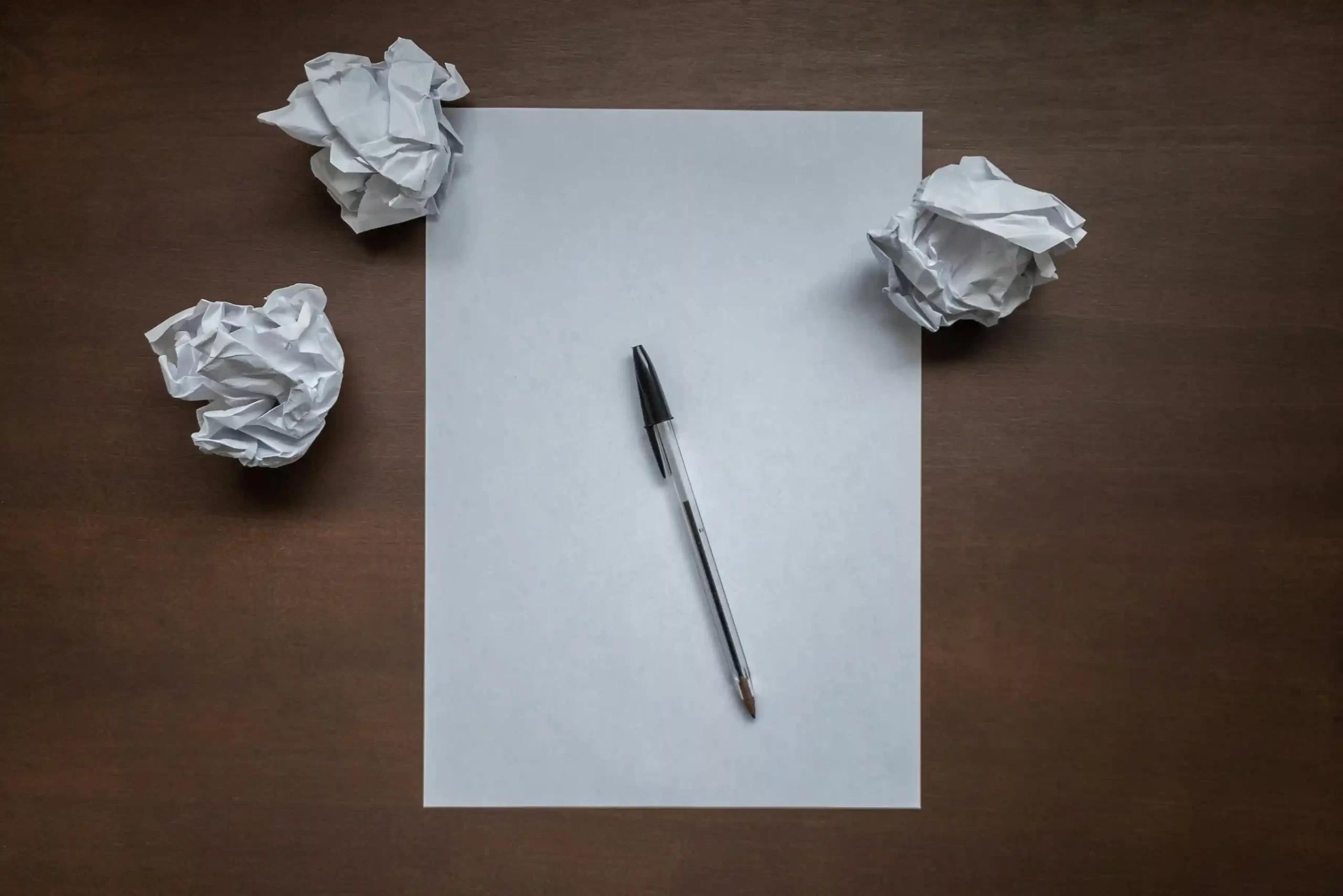 A blank piece of paper, a pen and three balled up sheets of paper