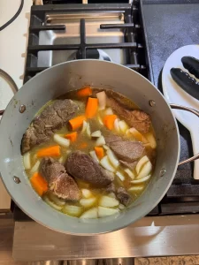 Short braised ribs, carrots and onions in a pot, cooking on the stove.