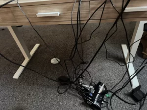 A desk with over 10 different cords tangled up underneath.