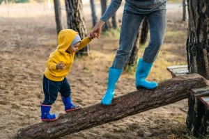 An adult's hand holding a toddler's hand while standing on a log, representing how a parent can balance homeschool activities while working full time