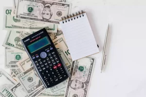 Various cash dollar bills, a notepad and a calculator on a table representing a budget for homeschool costs