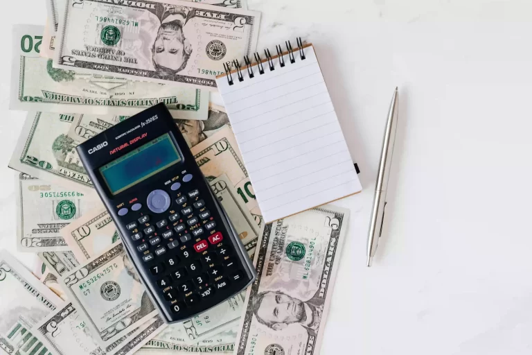 Various cash dollar bills, a notepad and a calculator on a table representing a budget for homeschool costs