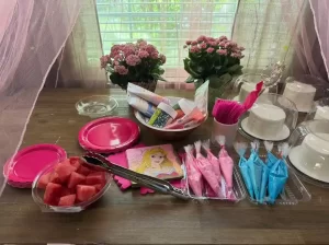 a dining room table with small white cakes and blue and pink bags of icing