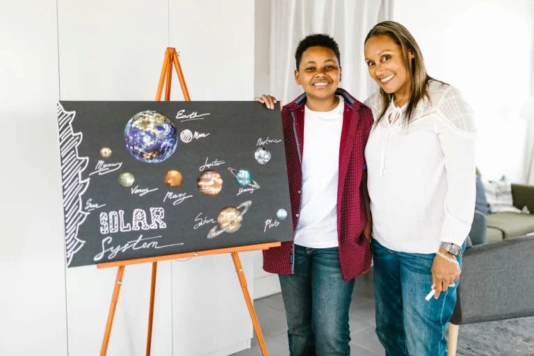 A mother with her preteen standing beside a solar system posterboard, representing the teach back facilitation homeschool technique