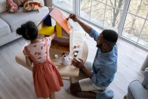 Christmas at-home activity with a father and daughter painting a wooden house