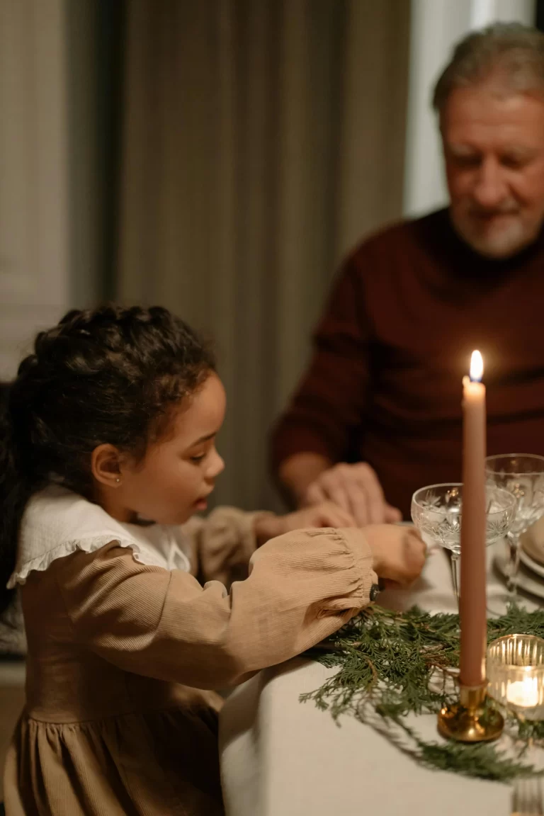 A young girl sitting at a table, wearing a vintage peter pan collar dress. The picture represents simple traditions for families.