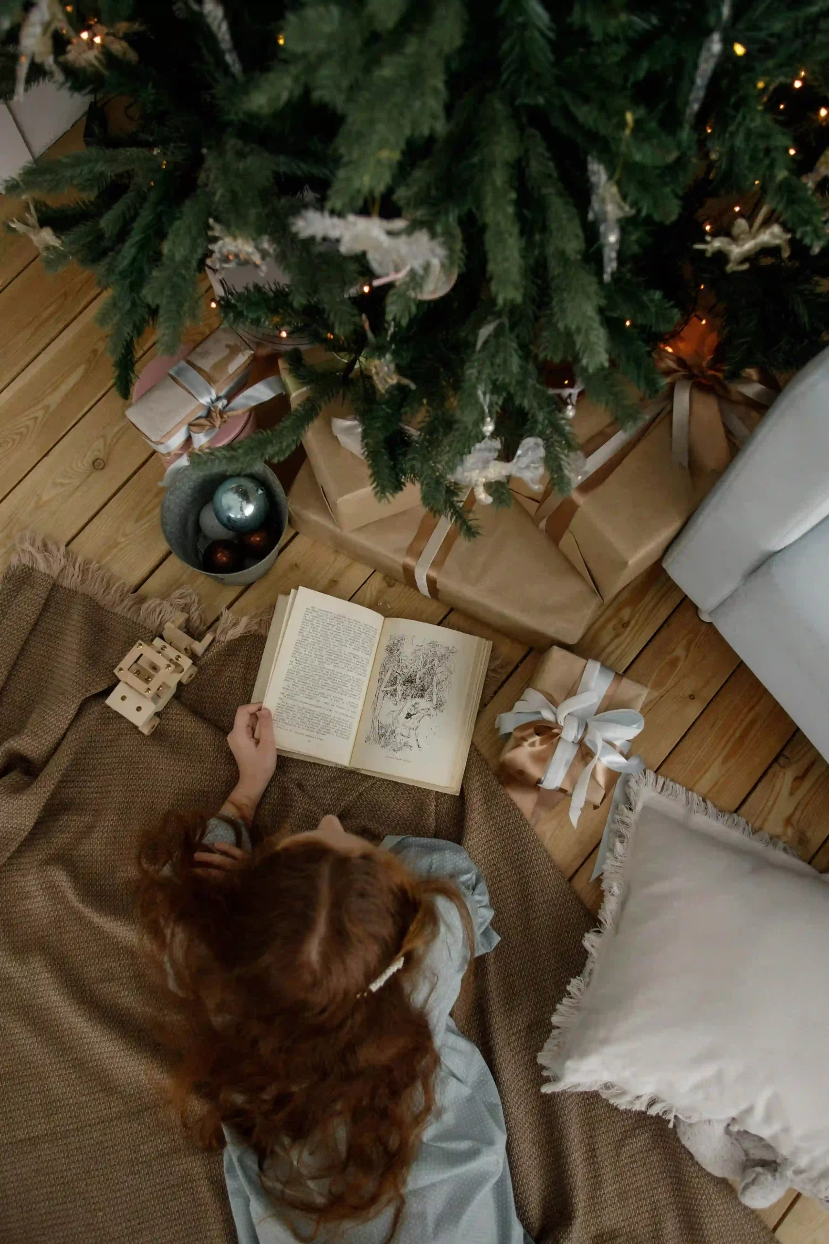 A young child reading a book underneath a Christmas tree, representing ideas for Christmas Eve boxes
