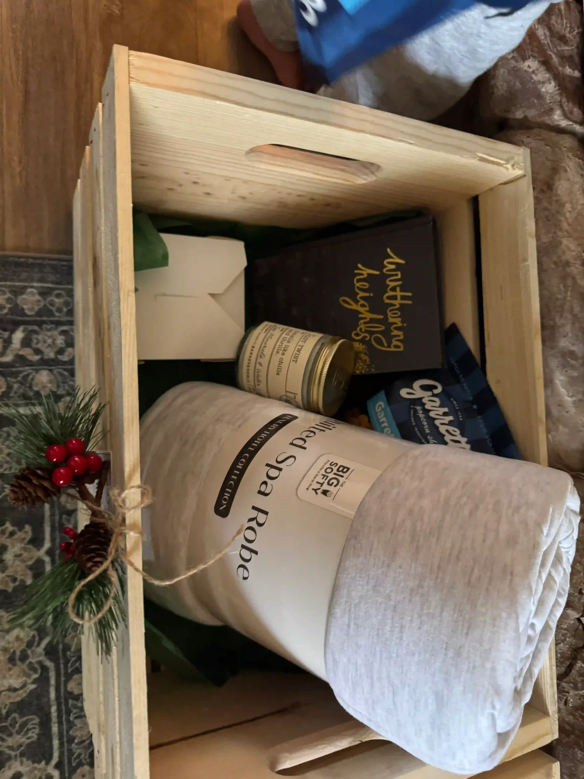 A wooden crate box containing a bathrobe, candle and a book. Represents Christmas Eve box ideas.
