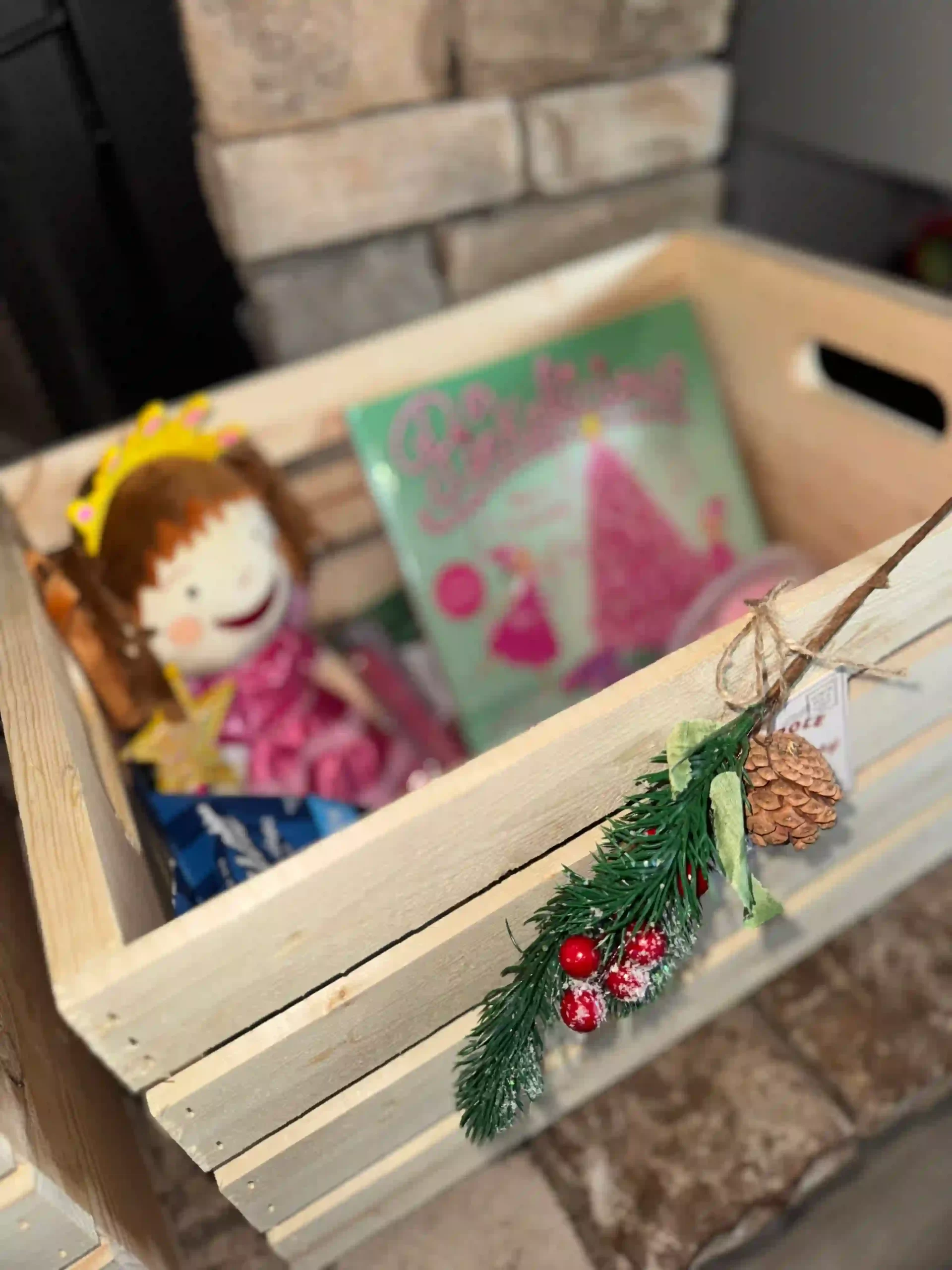 A wooden crate box with a pink doll and a book, representing Christmas Eve box traditions.