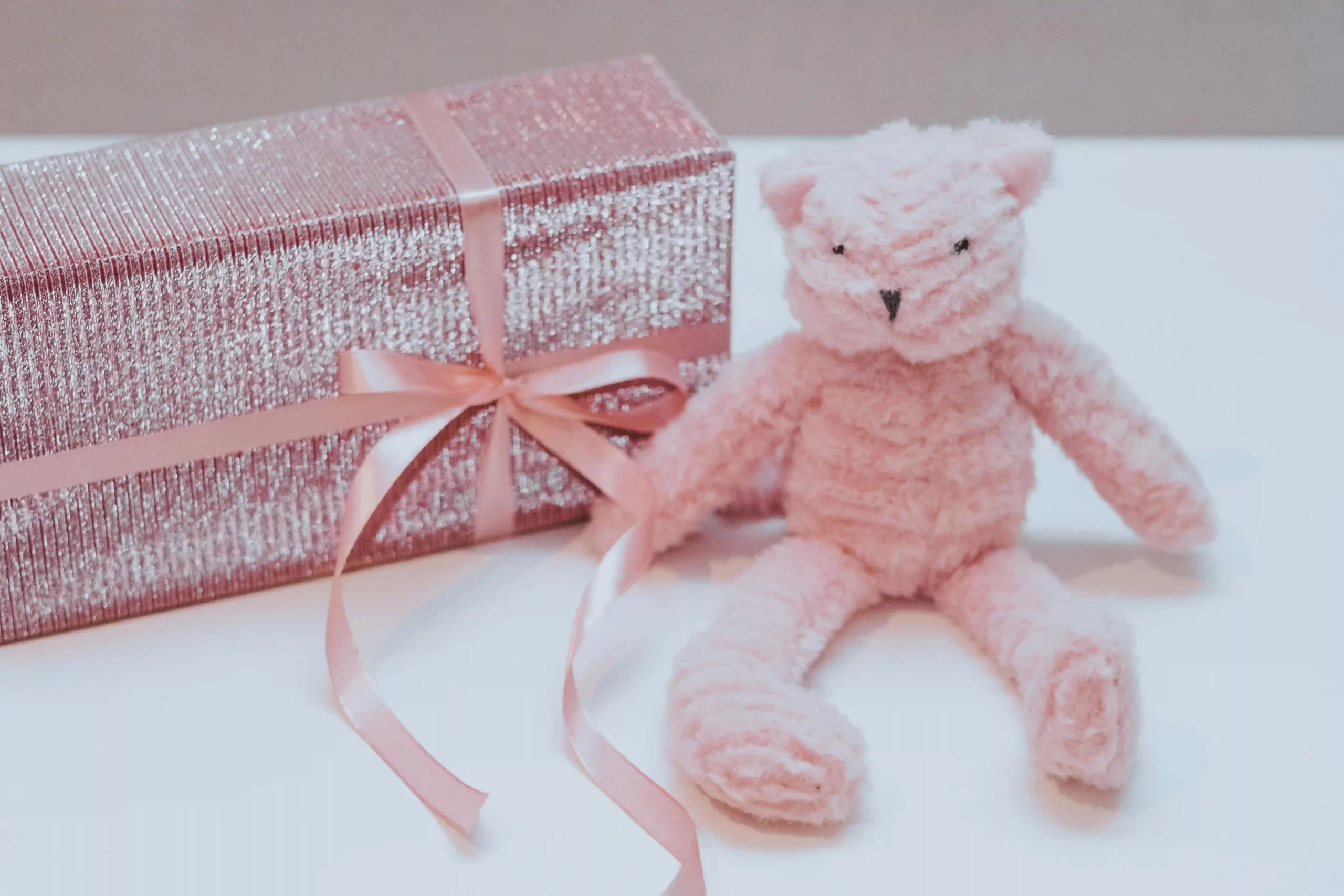 A pink teddy bear next to a sparkly pink gift box, representing experience-based gifts