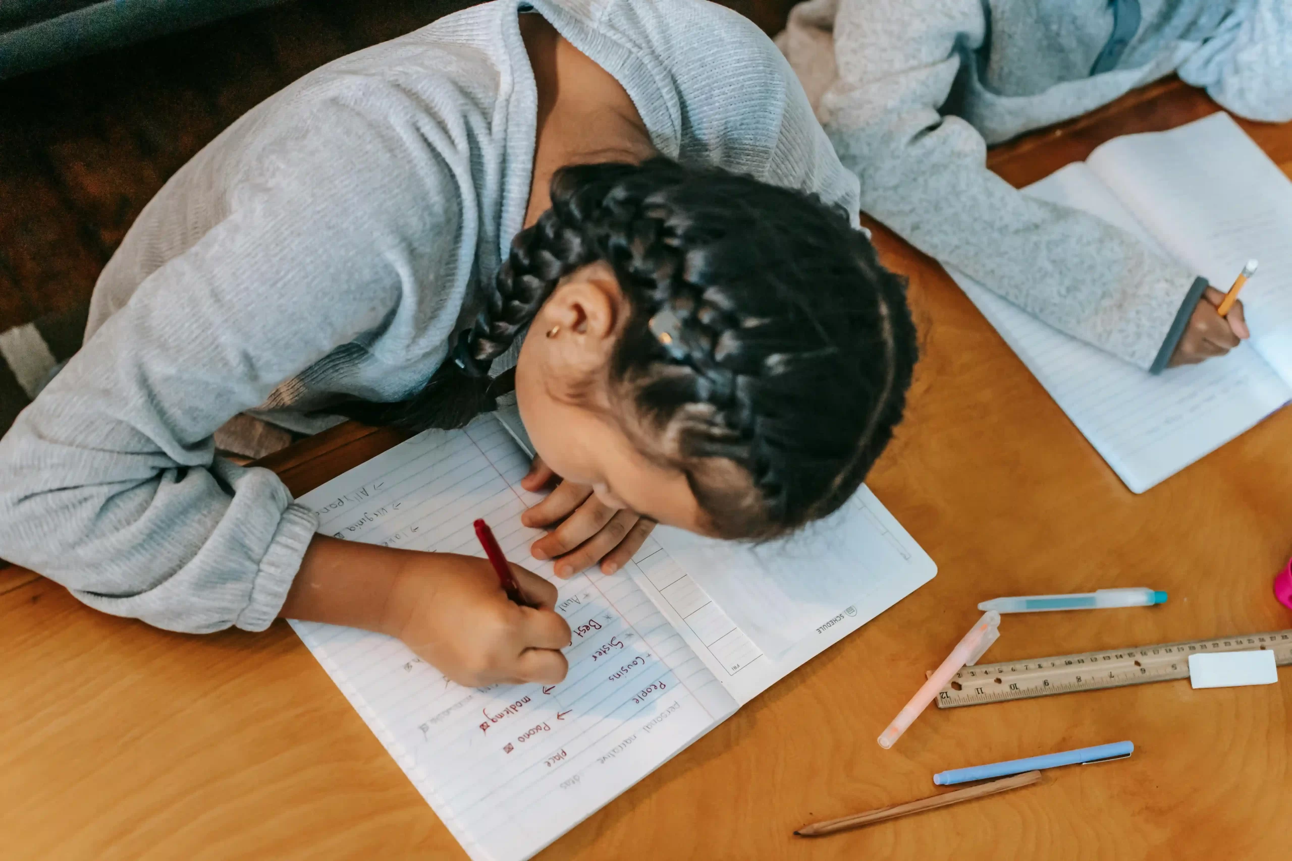 A young girl with french braids writing on a piece of paper, representing a homeschool monthly schedule