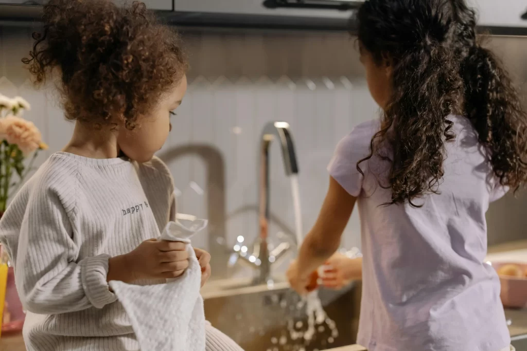 Two young girls doing dishes, representing chores by age